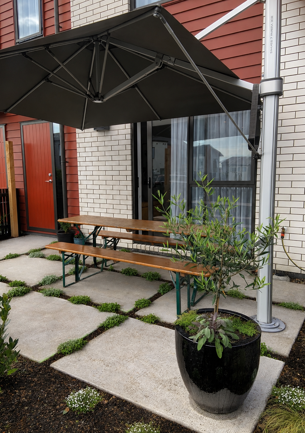 Courtyard with umbrella shade over timber bench seating, concrete pavers with groundcover planting